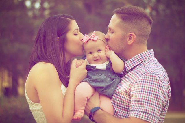 A couple is holding and kissing their child