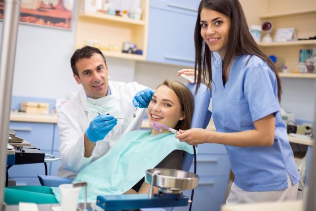 A female dental assistant is assisting the dentist with a patient