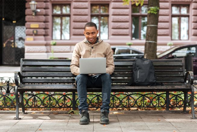 Online student sitting on a bench with laptop.