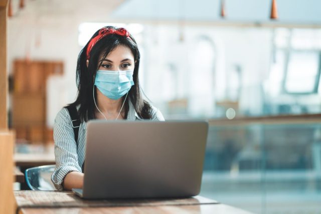 A female student is studying on her laptop with a mask on