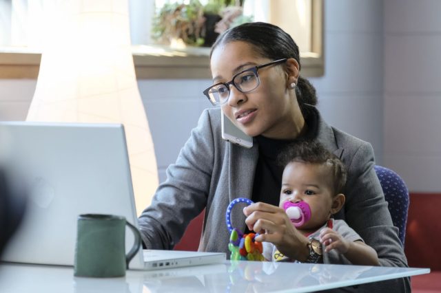 A parent is with her child at her work desk and on the phone